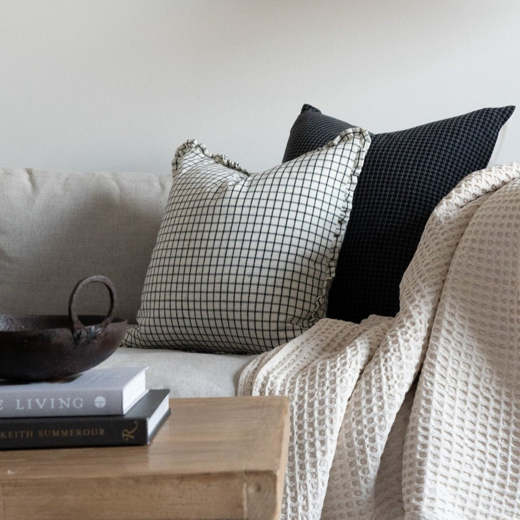 White and black grid ruffle pillow styled on neutral couch with dark accent pillow.