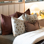 Floral block print pillow covers with green vines on beige linen styled on bed with brown accent pillows and gingham ruffle pillow.