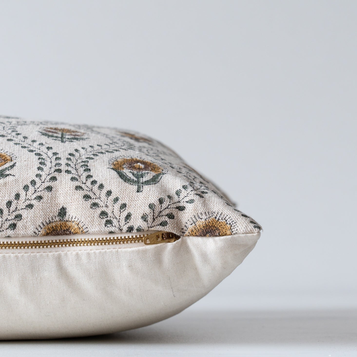 Floral block print pillow cover with beige linen backing and brass exposed zipper closure.